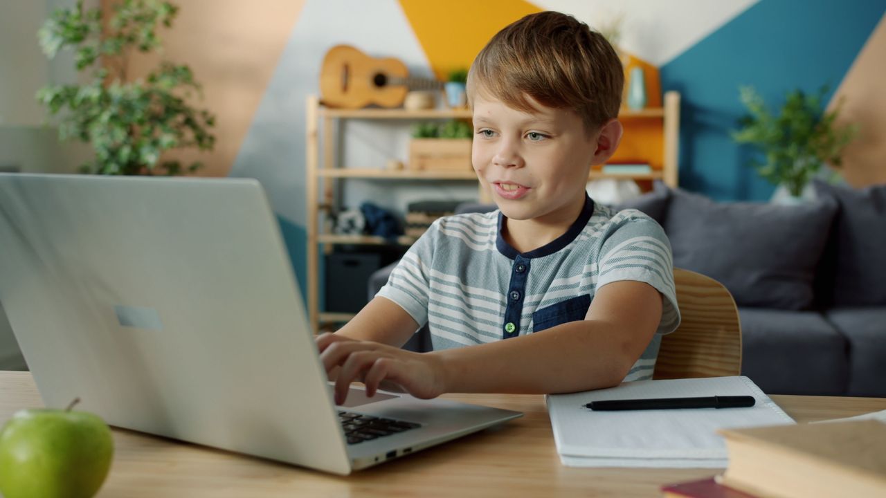 Young boy using a laptop for online learning at home with study materials nearby.