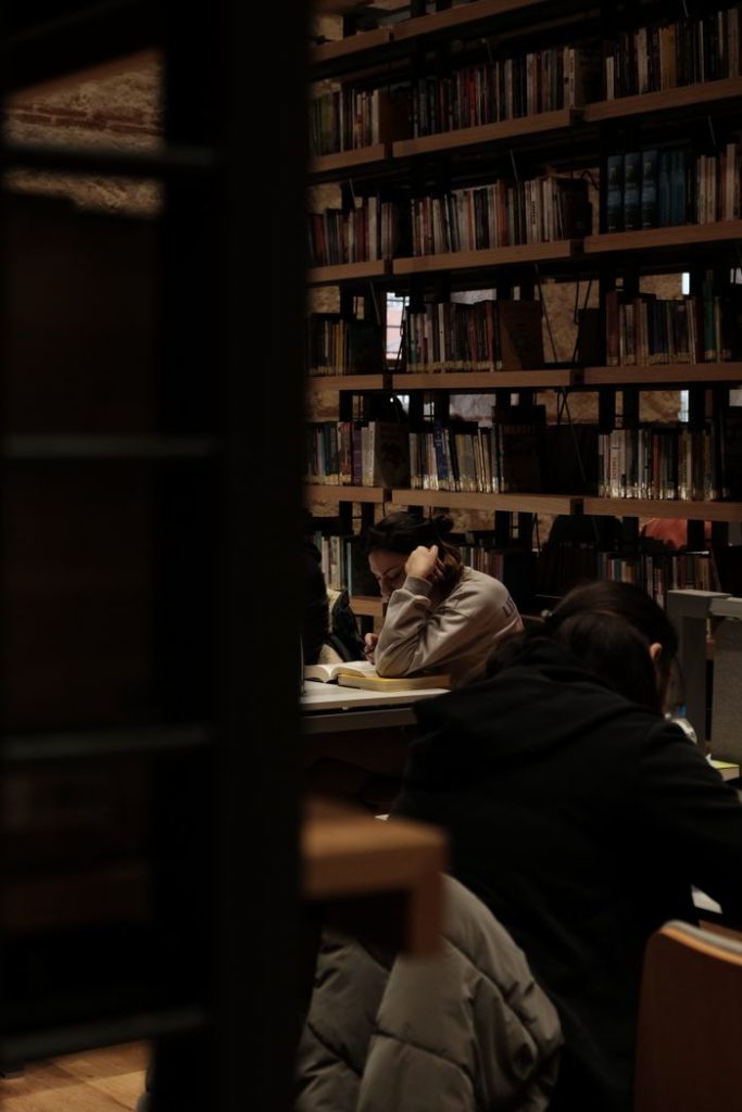 Quiet library scene with people reading and studying in a warmly lit environment.