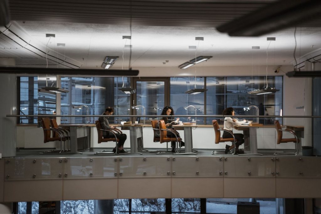 Adults studying in a modern library setting with large windows and ample lighting.